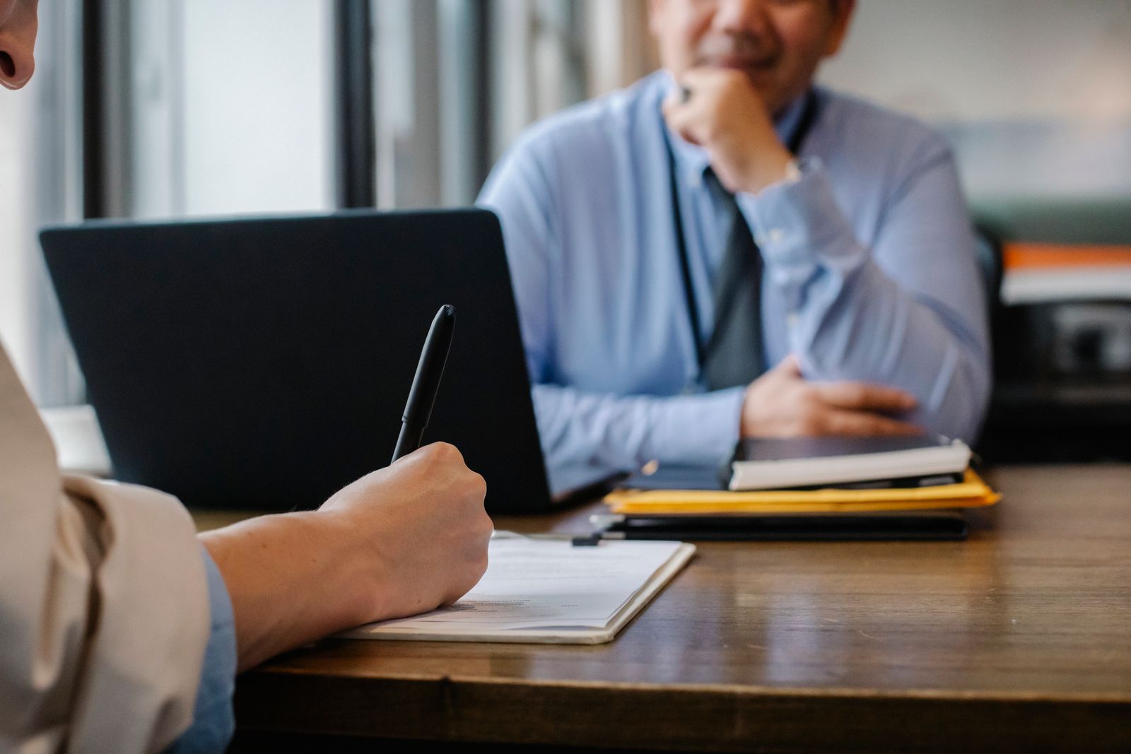 A person signing papers at a desk while another person looks on. Photo: Sora Shimazaki / Pexels